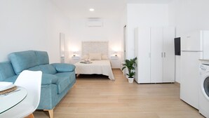 A modern, well-lit room with a bed, a blue sofa, a small dining table, and a washing machine. - Studio Apartment 'Apartamentos Maria' with Wi-Fi and Air Conditioning (Vejer de la Frontera)