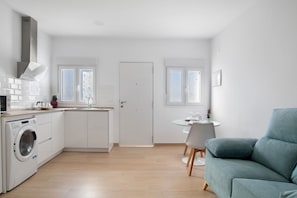 Une cuisine compacte équipée d’un lave-linge, un coin repas avec une table et des chaises, et un canapé bleu.