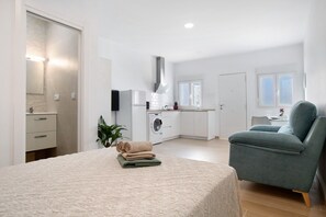Une chambre moderne avec un lit, un fauteuil vert, un lave-linge et un coin cuisine.