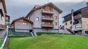 Un edificio de varios pisos con balcones, fachada de piedra y un espacio verde delantero.