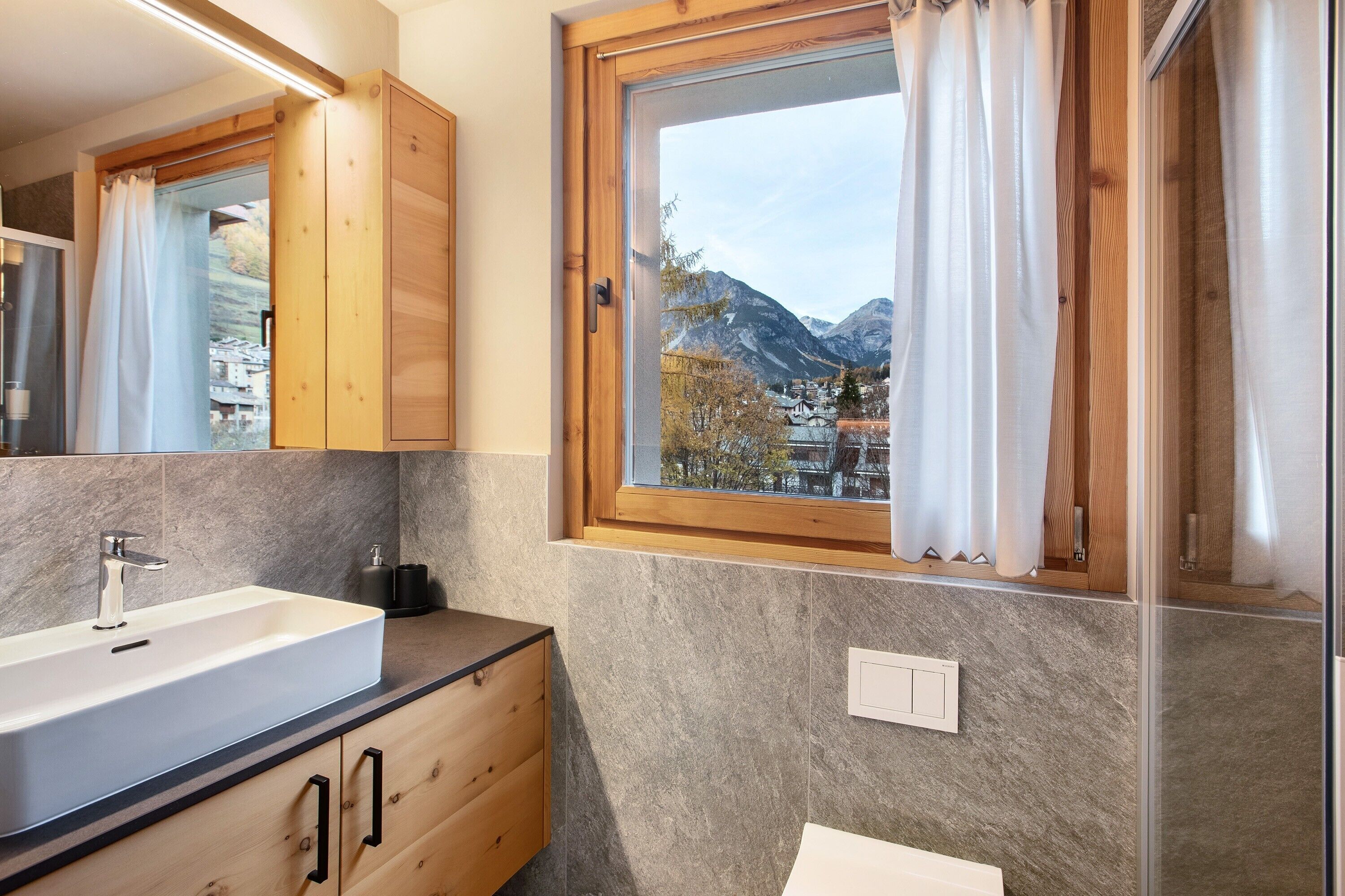 Ein Badezimmer mit einem großen Waschbecken, Holzausbau, einem Fenster mit Vorhängen und Bergblick.