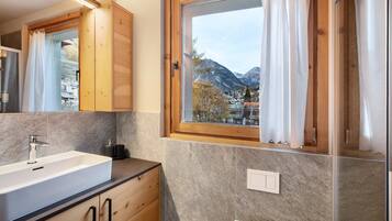 Ein Badezimmer mit einem großen Waschbecken, Holzausbau, einem Fenster mit Vorhängen und Bergblick.