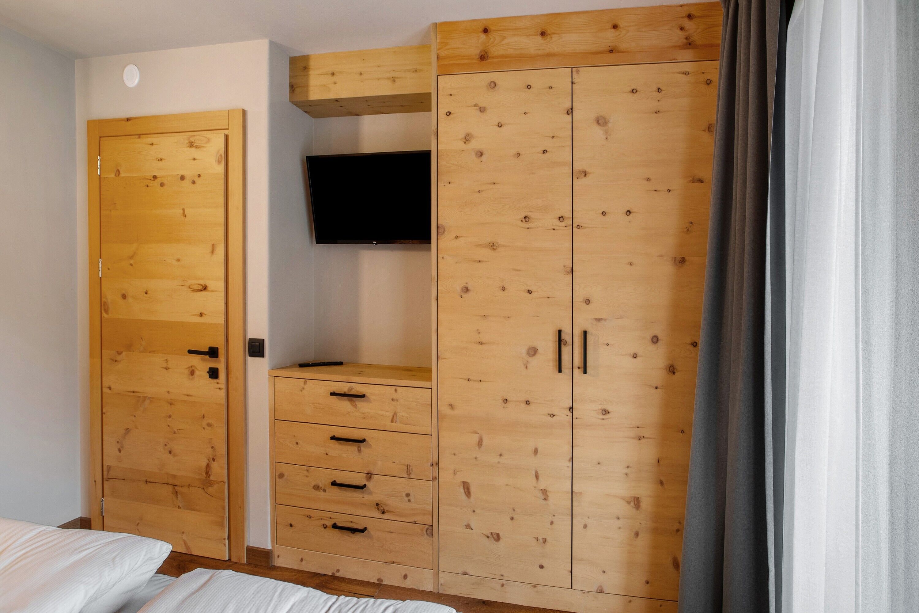 Una camera da letto con un'armadiatura in legno, una televisione montata a parete e un letto.