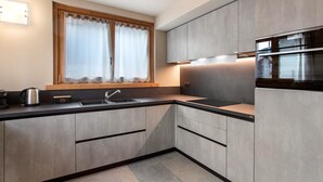 Una cocina moderna con armarios grises, un lavamanos de acero inoxidable y una ventana con cortinas.