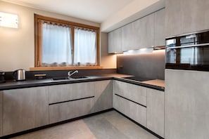 Eine moderne Küche mit grauen Schränken, einer Edelstahlspüle und einem Fenster mit Vorhängen.