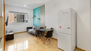 Un espacio habitable compacto con kitchenette, zona de comedor con mesa y sillas, sofá y refrigerador.