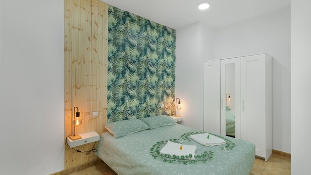 Un dormitorio con cama, mesitas de noche, un armario y una pared con diseño de hojas.