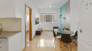Una cocina moderna con un fregadero, una zona de comedor con mesa y sillas, un sofá y un televisor montado en la pared.