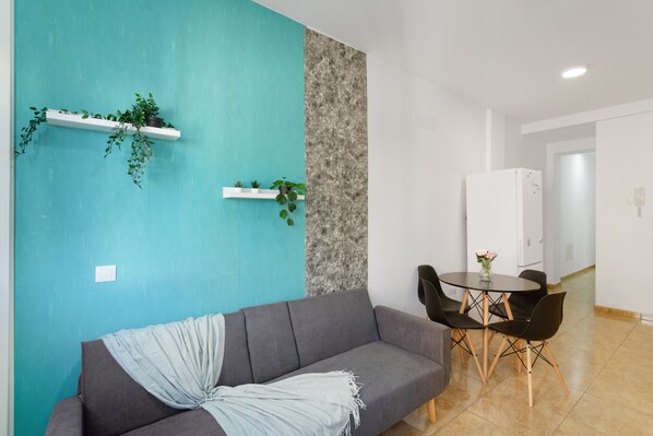 A modern living room with a grey sofa, a teal accent wall, and a dining area with a table and chairs.