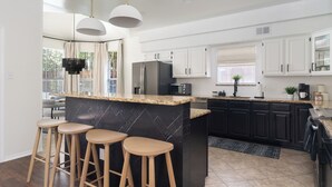 Een moderne keuken met een centraal eiland, barkrukken, witte kasten en een zwart marmeren aanrecht.