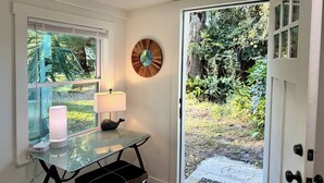 A room with a glass table, a lamp, a decorative wall piece, and a door leading to a garden. - Private marsh views -under mossy oaks, minutes to beaches & downtown’s  (Fernandina Beach)