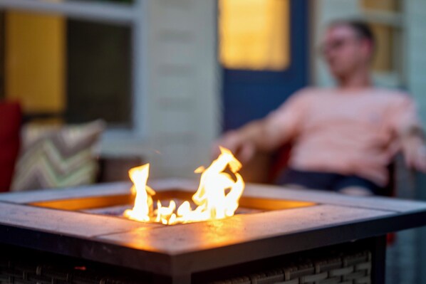 Une cheminée avec des flammes, une personne assise sur un canapé et une fenêtre en arrière-plan.