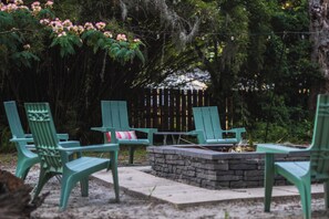 Un espace patio avec des chaises vertes, un foyer en pierre et une clôture en bois en arrière-plan.