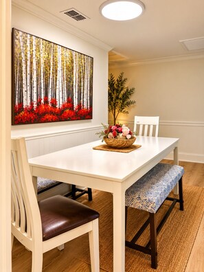 A dining area with a white table, two chairs, a bench, a painting of a forest, and a decorative plant. - Private marsh views -under mossy oaks, minutes to beaches & downtown (Fernandina Beach)