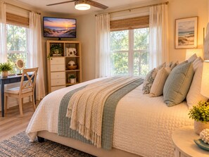 A bedroom with a large bed, a desk, a chair, a television, and a bookshelf.