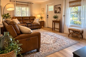 A living room with a brown leather sofa, a patterned rug, and a wicker stool.