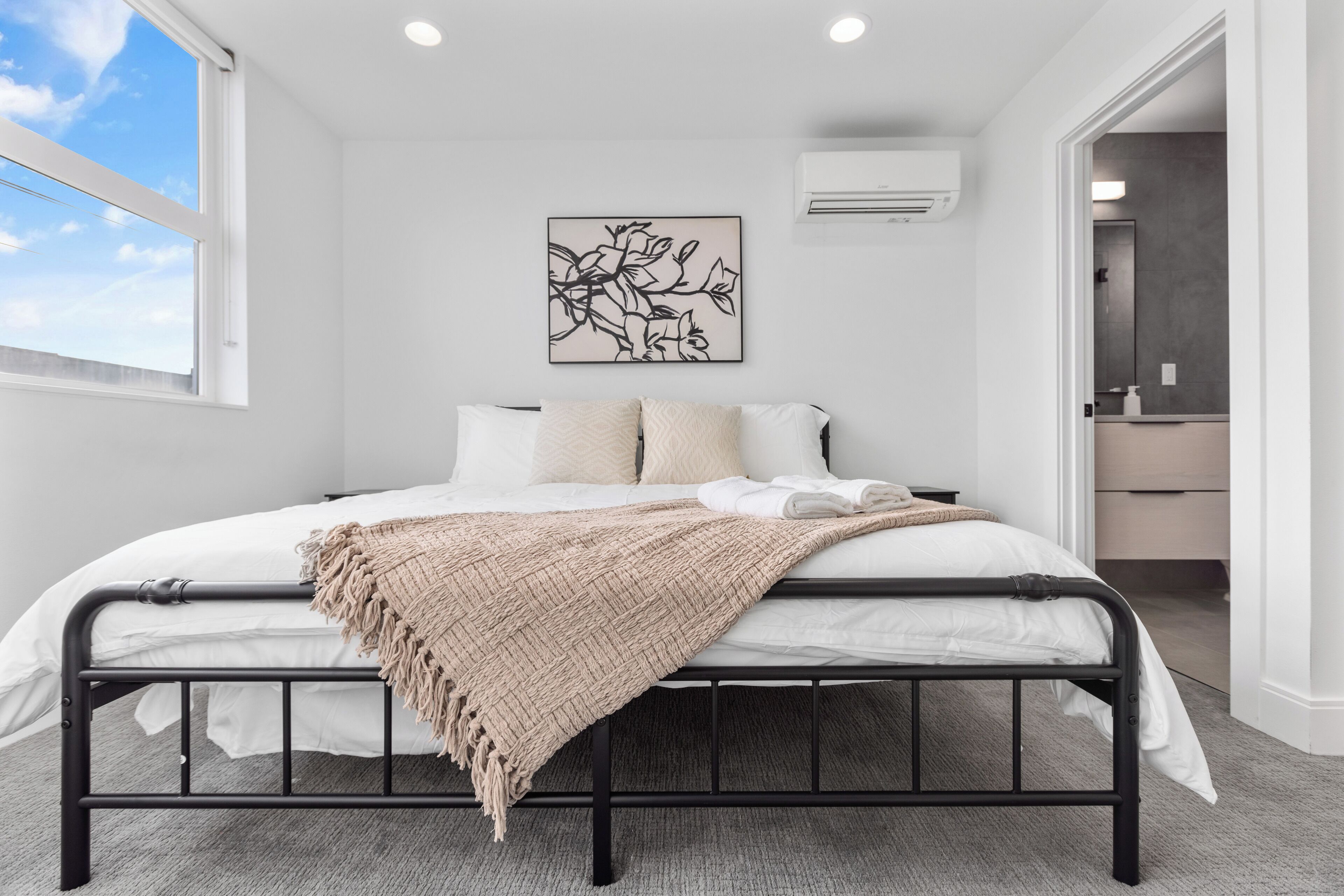 Ein Schlafzimmer mit Bett, Fenster, Wandklimaanlage und einem gerahmten Kunstwerk.