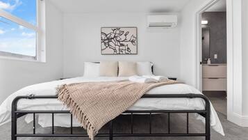 Ein Schlafzimmer mit Bett, Fenster, Wandklimaanlage und einem gerahmten Kunstwerk.