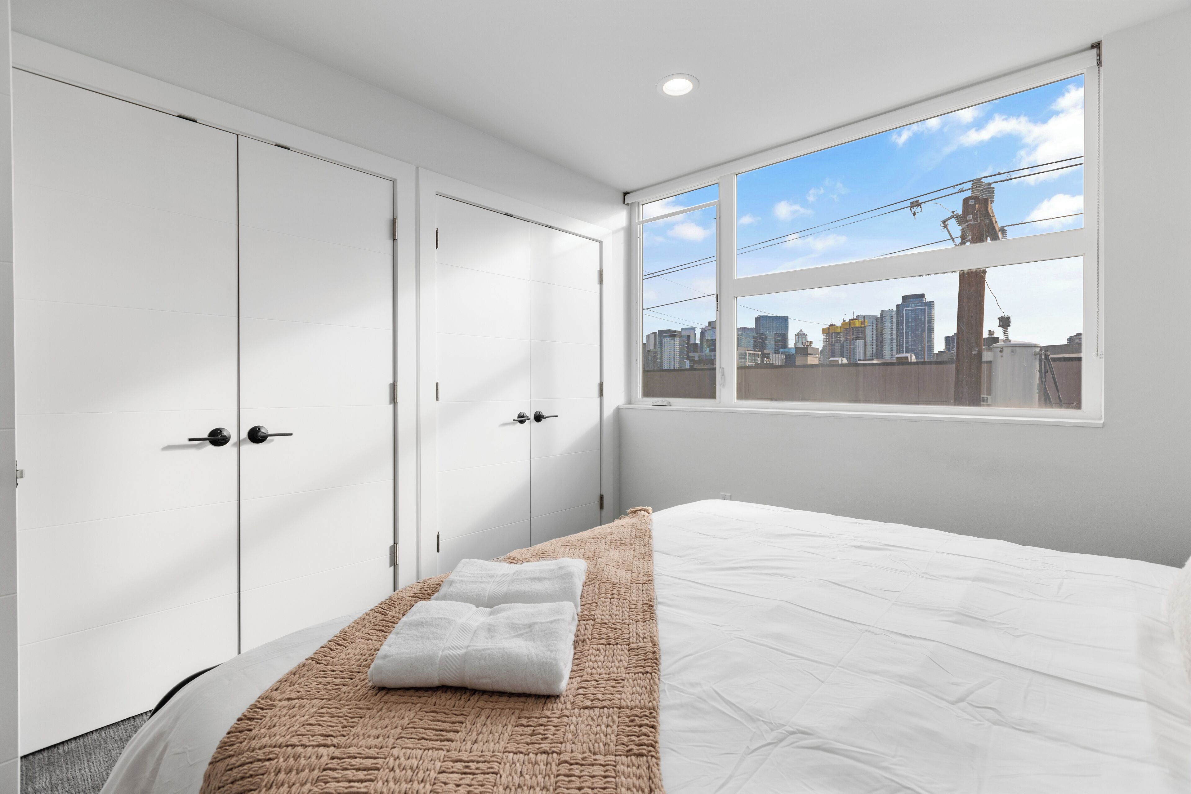 Quarto de hotel moderno com uma cama grande, vista para o horizonte da cidade e armários brancos.