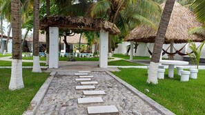 A pathway leading to a thatched-roof structure surrounded by palm trees and white columns.