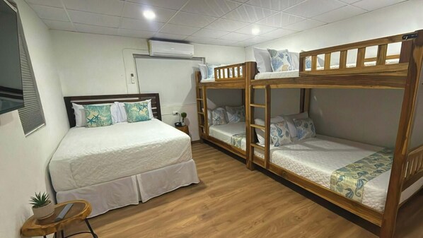 A room with a large bed, a bunk bed, a small table with a plant, and an air conditioning unit on the wall.