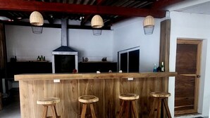 Un espace bar avec un comptoir en bois, quatre tabourets et des lampes suspendues en osier.