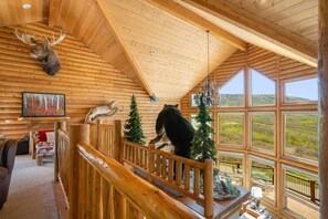 A log cabin interior with a wooden staircase, a bear statue, a deer head, and a painting of a forest. - Mountain Haus: Hot Tub, Views & Ski Access (Mesa)