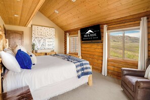 Une chambre aménagée dans un chalet en rondins, avec un grand lit, un plafond en bois et une vue sur les montagnes par la fenêtre.