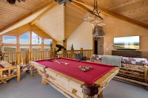 A cozy room with a pool table, wooden furniture, and a large TV.