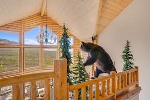 Um urso em um corrimão de madeira, com vista para uma paisagem deslumbrante através de grandes janelas.