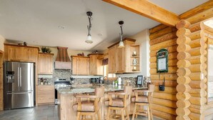 Eine moderne Küche mit Holdekor, einem Edelstahl-Kühlschrank, einer großen Kücheninsel mit Barhocker und einer Wand aus Holz.