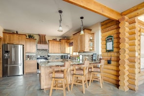 Eine moderne Küche mit Holdekor, einem Edelstahl-Kühlschrank, einer großen Kücheninsel mit Barhocker und einer Wand aus Holz.