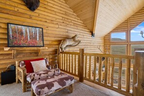 A log cabin interior with a bed, a painting, and a mounted animal head.