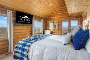 Ein Schlafzimmer in einer Blockhütte mit einem Bett, einem Wandzeichen mit der Aufschrift 'SKI & RIDE MOUNTAIN HAU' und einem Fenster mit Bergblick.