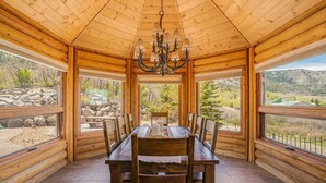 Ein Esszimmer mit Holzboden, einem Kronleuchter, großen Fenstern und Blick ins Freie.