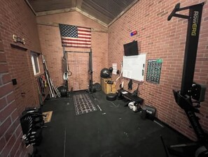A gym with brick walls, an American flag, weightlifting equipment, and a whiteboard. - Bar, pool table, dart board and 2 bedrooms, what else do you need? (Redmond)