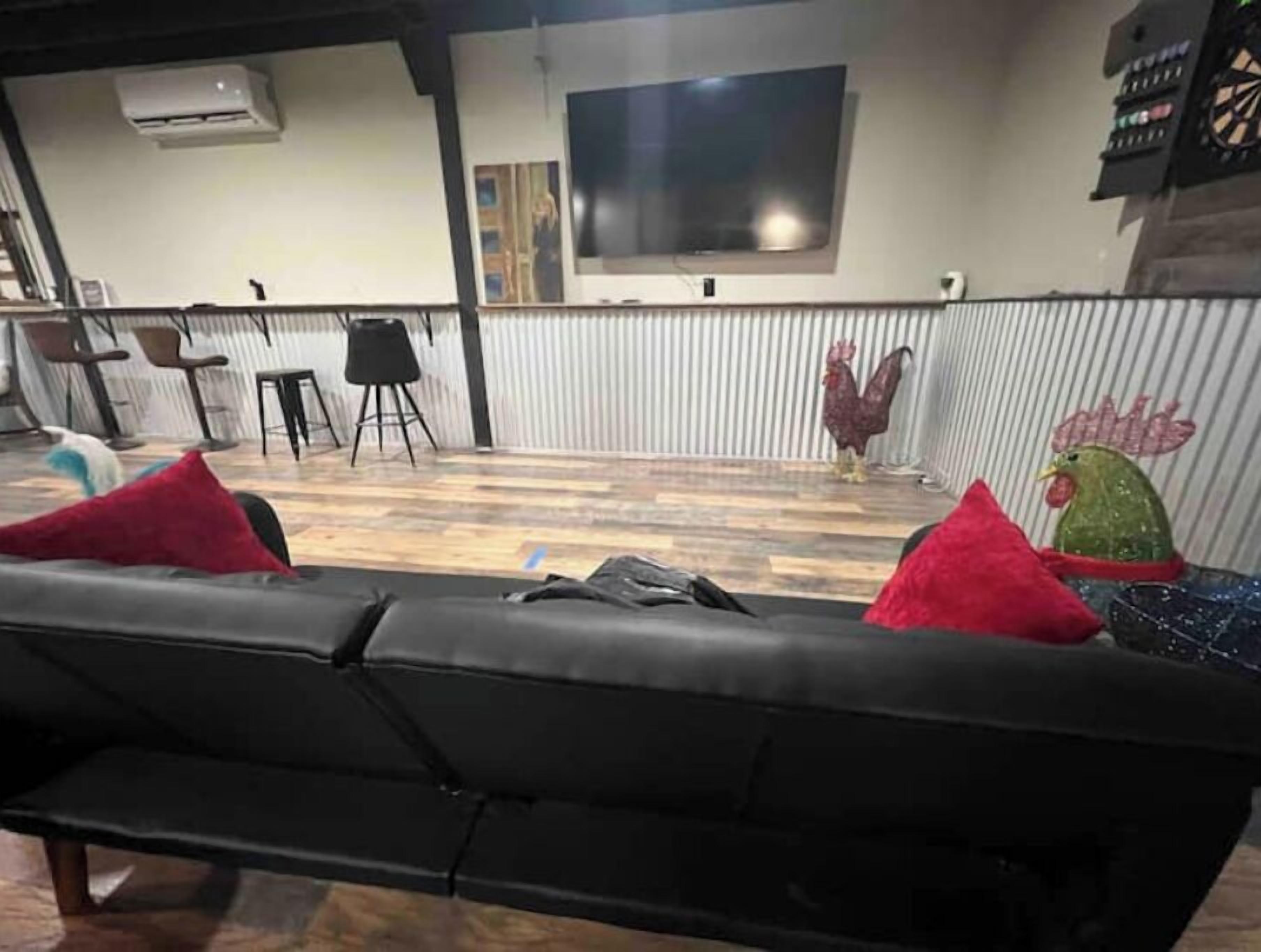 Een moderne woonkamer met een zwarte bank, rode kussens, een aan de muur bevestigde televisie en een houten vloer.