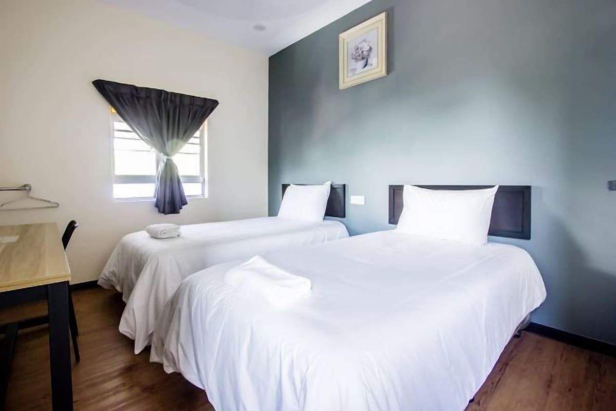 Habitación de hotel con dos camas, una mesa de madera y un ventanal con cortinas.