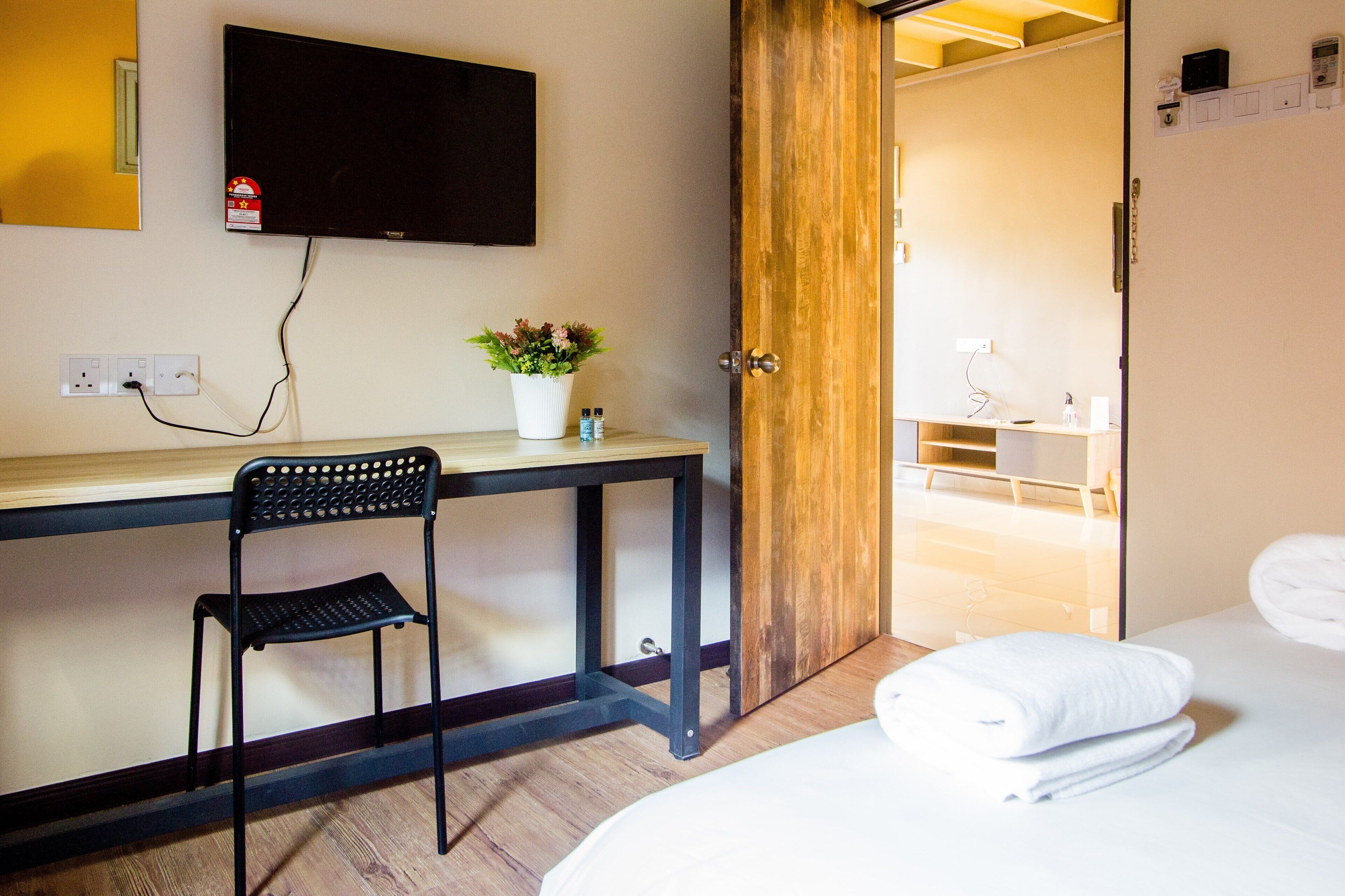 Une chambre d’hôtel avec un lit, un bureau et une chaise, une télévision, une plante et une salle de bain visible à travers une porte ouverte.