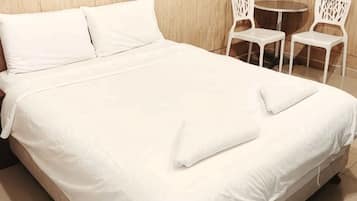 Een opgemaakt bed met witte lakens, een klein rond tafeltje en twee witte stoelen in een kamer met houten wanden.