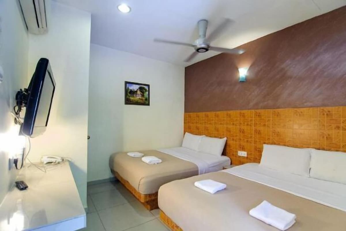 Une chambre d’hôtel avec deux lits, un téléviseur à écran plat, un ventilateur de plafond et une petite table avec un téléphone.