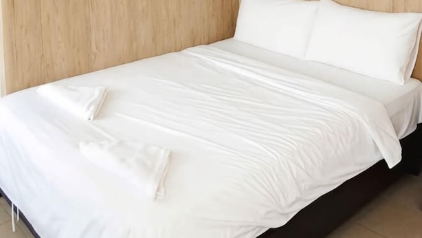 A neatly made bed with white linens and pillows, a wooden headboard, and a clean, uncluttered room.