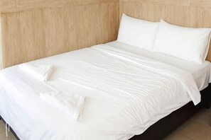 Ein ordentlich bezogenes Bett mit weißen Leinen und Kissen, ein hölzernes Kopfende und ein sauberer, aufgeräumter Raum.