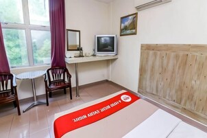 Quarto com cama, escrivaninha com computador, cadeira, janela com cortinas e radiador.