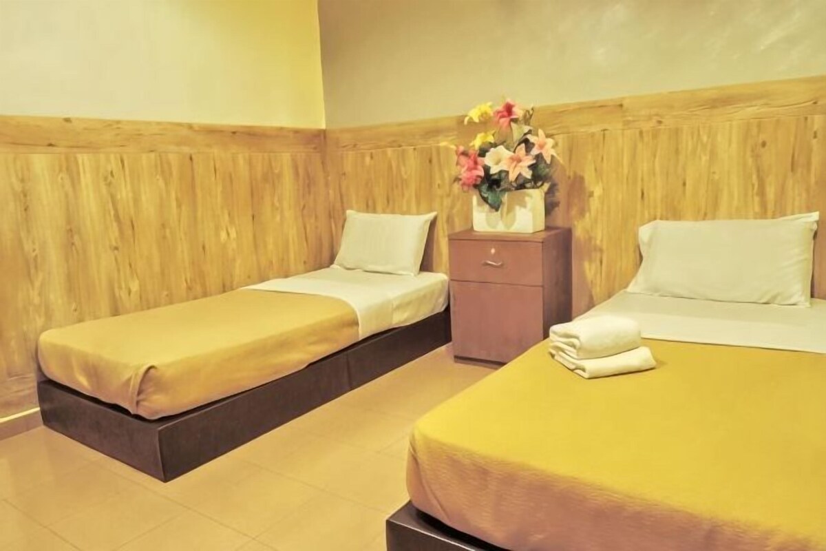 Ein Hotelzimmer mit zwei Betten, einem Holz-Kopfteil, einem Nachttisch und einer Vase mit Blumen.