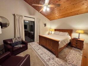 Une chambre avec un plafond en bois, un lit, une table de chevet, une chaise, une lampe, un miroir et un tapis à motifs.