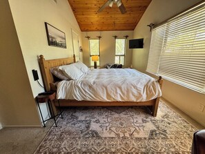 Quarto com cama de madeira, tapete estampado, ventilador de teto e janela com persianas.