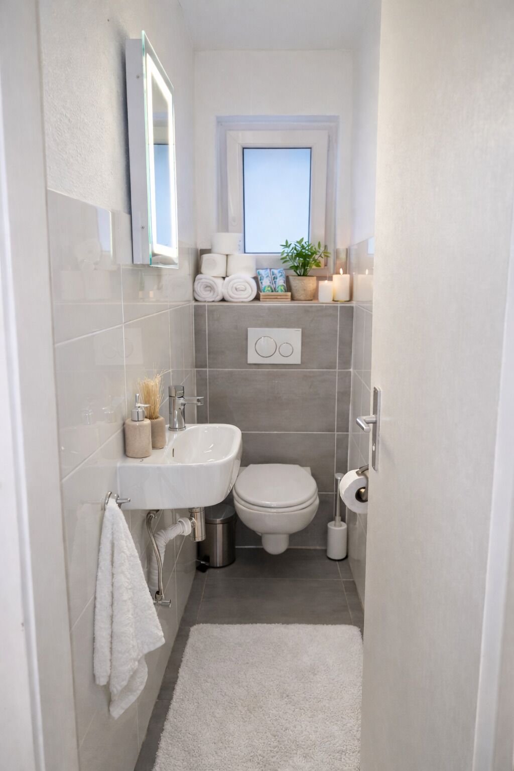 A compact bathroom with a white sink, toilet, and a small window above the toilet.
