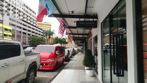 Een hotelgang met geparkeerde voertuigen, een potplant en een bord met 'The Daily Hotel'.