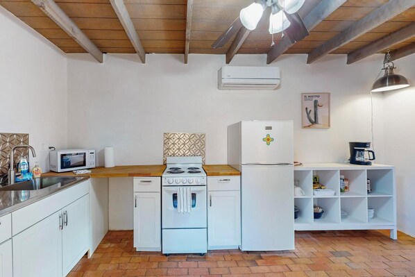 Una cocina compacta con muebles blancos, un microondas, una estufa y un refrigerador.
